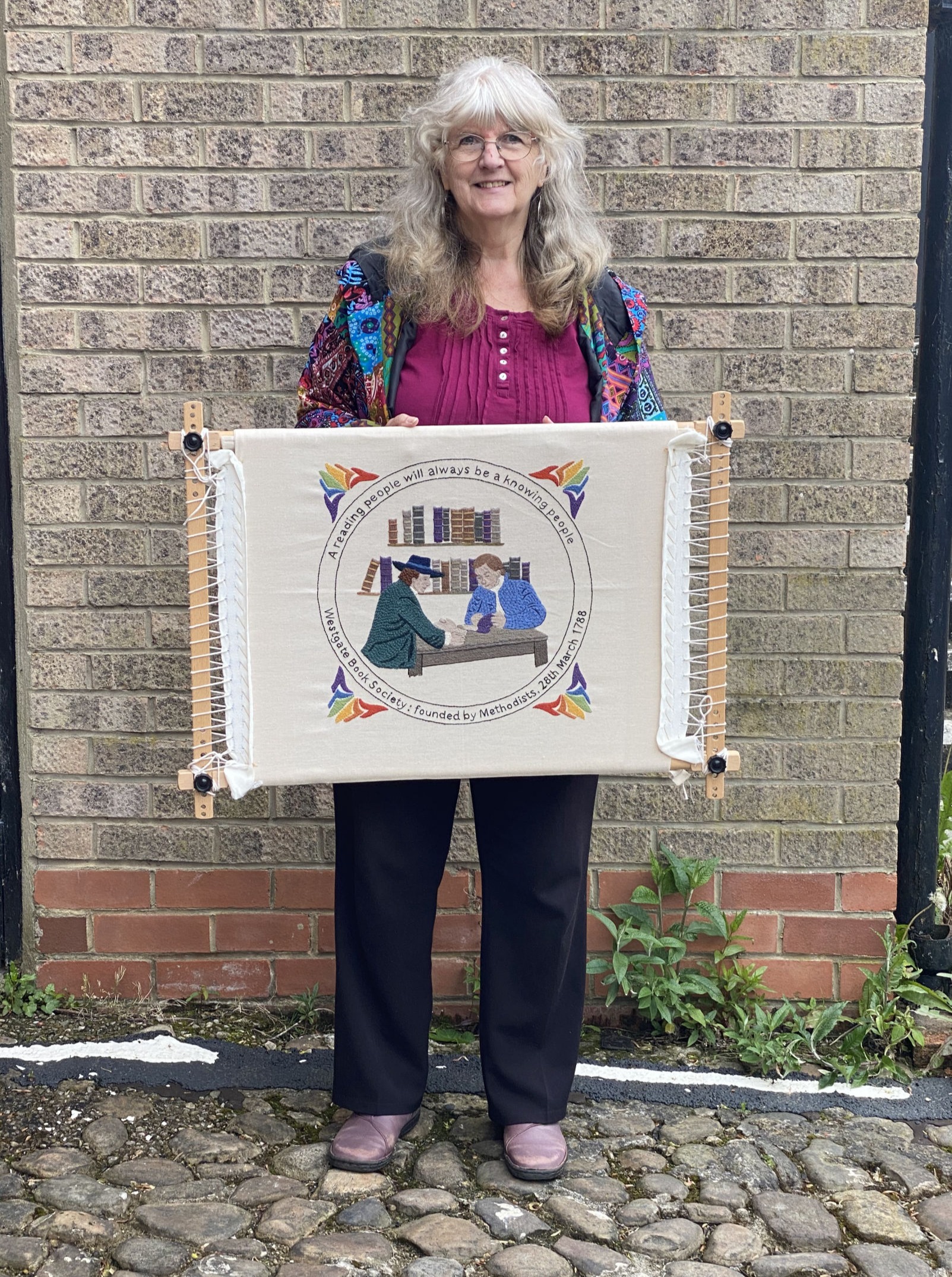 Victoria the stitcher holding the finished tapestry
